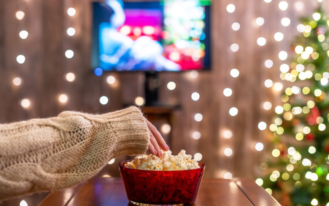 A woman eating popcorn and watching TV in a room decorated for Christmas.