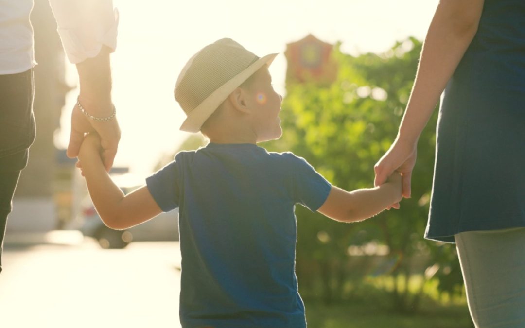 A family with a young child holding hands outdoors.